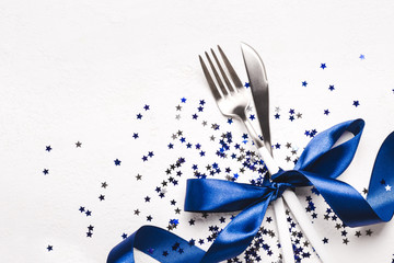 Christmas cutlery with phantom blue ribbon and stars confetti on white background