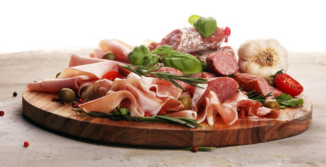 Food tray with delicious salami, pieces of sliced prosciutto crudo, sausage and basil. Meat platter