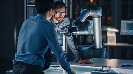 Diverse Team of Engineers Analyse and Discuss How a Futuristic Robotic Arm Works and Moves a Metal...