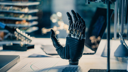 Close Up of a Futuristic Prosthetic Robot Arm Stands on a Desk in a High Tech Research Laboratory with Modern Computer Equipment.