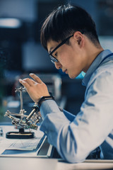 Vertical Shot of a Professional Japanese Electronics Development Engineer in Blue Shirt is Soldering a Circuit Board in a High Tech Research Laboratory with Modern Computer Equipment.