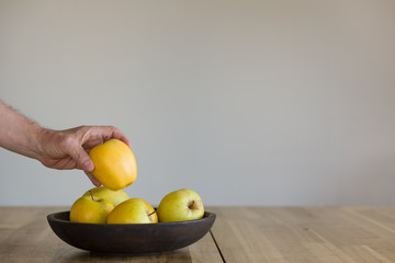 A man's hand takes a Yellow Apple from a wooden bowl. Concept of healthy food and eco-friendly living environment.