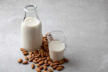 Almond drink milk in glass bottle surrounded by almonds nuts