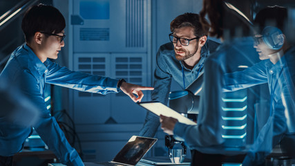 Diverse Team of Engineers with Laptop and a Tablet Analyse and Discuss How a Futuristic Robotic Arm...