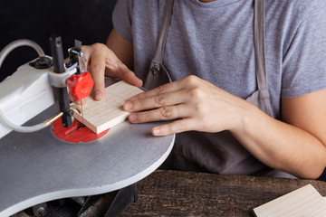 A girl carves a Christmas tree toy on a jigsaw from a tree.