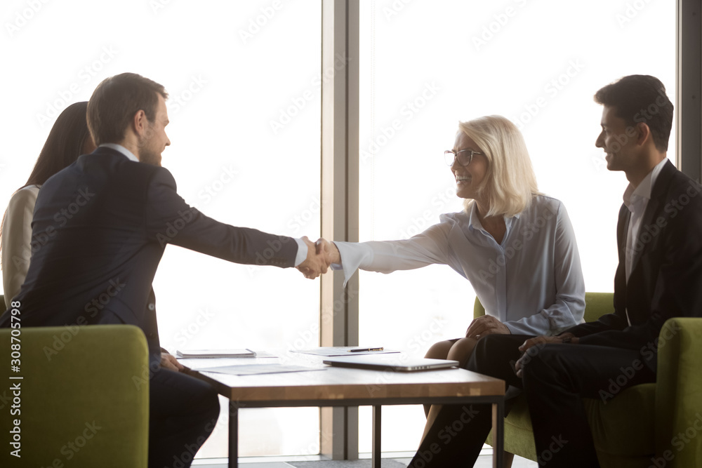 Sticker Smiling mature businesswoman shaking hand of business partner at meeting