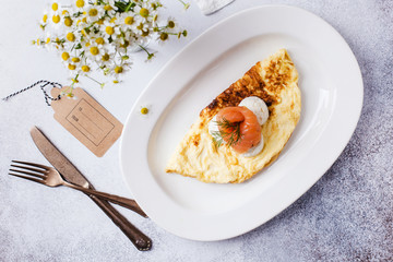  Breakfast time. Omelet with red fish and daisies in a vase on a light gray table with a textured background.