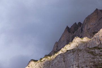 Beautiful view on stately alpine peak. Close up on high mountain on dark clouds background. Sunlight on rocky summit. Swiss alps.