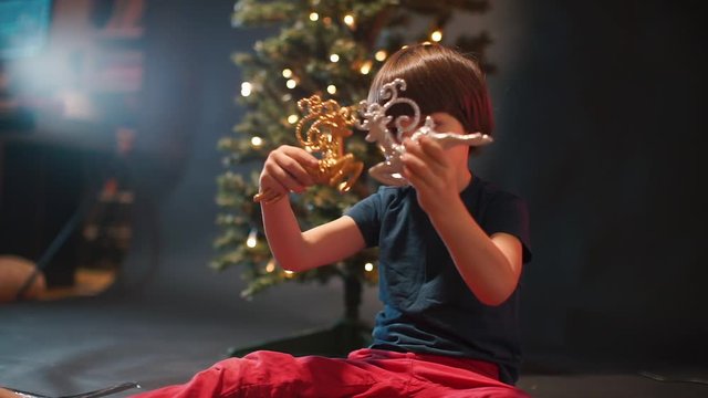 The child plays with toy deers near the New Year tree.