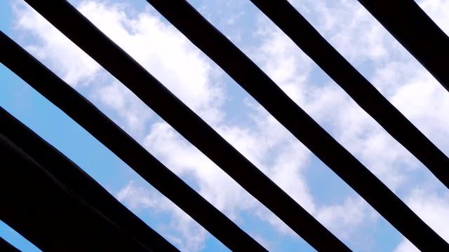 Low angle pov of clouds timelapse behind a wood pergola.
