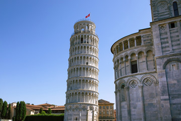 Fototapeta na wymiar Leaning Tower of Pisa with part of Cathedral of st Mary and surrounding buildings on the square. Blue sky, summertime, no people. Italy
