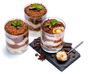 Classic tiramisu dessert in a glass cup on stone serving board and pieces of chocolate on white background with clipping path