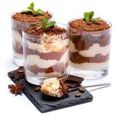 Classic tiramisu dessert in a glass cup on stone serving board and pieces of chocolate on white background with clipping path