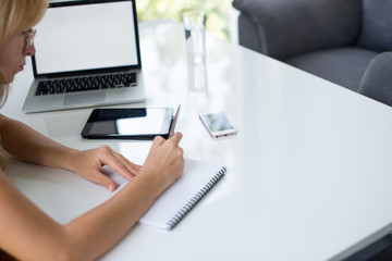 A blonde hair businesswoman working in her workstation. Businesswoman working at workplace. Woman working in home office. Woman sitting at desk and working with laptop and glass of water.