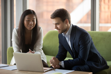 Smiling Asian businesswoman and businessman using laptop together