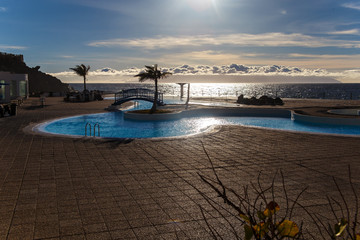 Place for vacationers on the popular resort Los Gigantes on the northwest coast of Tenerife island, Spain. There is La Gomera Island hidden by clouds on the horizon. Photo was taken against the sun.