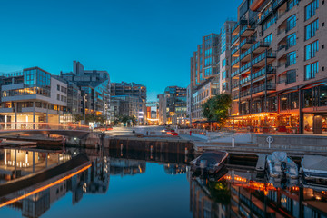 Oslo, Norway. Night View Embankment And Residential Multi-storey Houses In Aker Brygge District. Summer Evening. Residential Area Reflected In Sea Waters. Famous And Popular Place