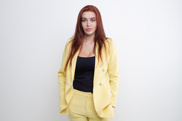 Beautiful girl with red hair posing in yellow business suit on white background