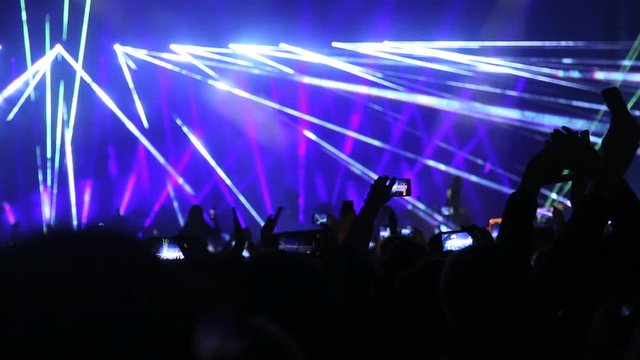 Crowd of spectators raises their hands up and applauds the musician performing on the stage. Silhouette hands of audience crowd people use smartphones enjoying the concert. Live music concert.