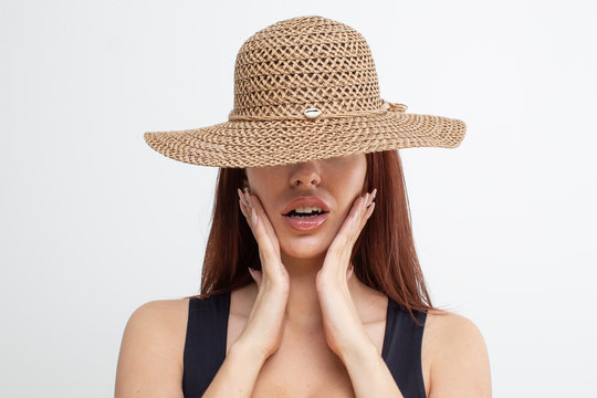 Red-haired girl in a black t-shirt and straw hat posing on a white background