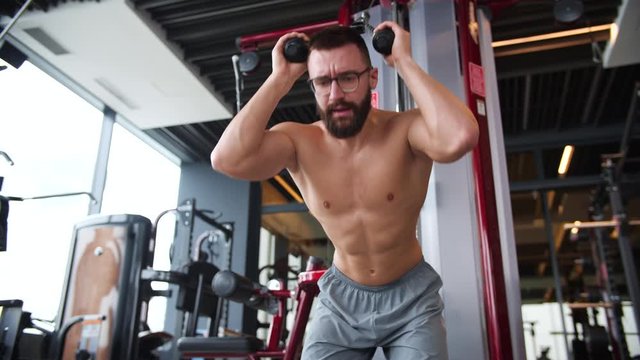 Young athletic man in gym training back muscles exercise using cable crossover machine.