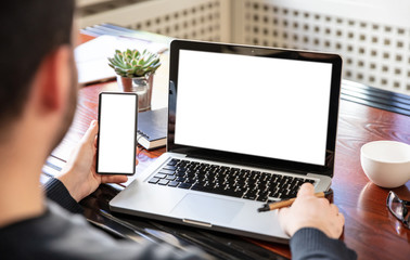 Laptop and smartphone with white blank screens, office interior background