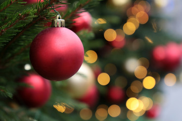 Red Christmas balls on a fir branches on festive lights background, night illumination. New Year tree with colorful decorations, magic of winter holiday