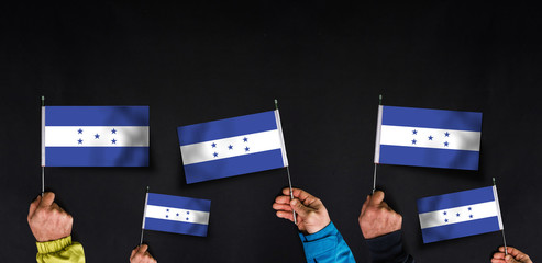 Hands holds flags of Honduras on dark background