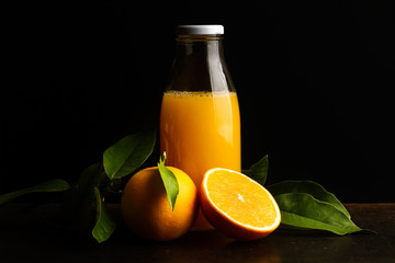 Botella con zumo de naranjas, naranja entera y por la mitad sobre mesa oscura rústica. Vista de frente. Copy space