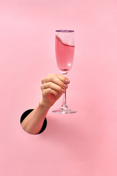 Naklejki Kieliszek do wina różanego w kobiecej dłoni z dziury w ścianie.