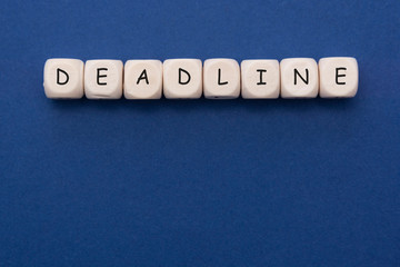 Deadline word on wood blocks over blue background with copy space.