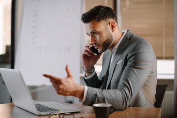 Fototapeta premium Handsome businessman in office talking on phone. Successful man in suit discussing business on phone call. 