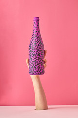 Painted hot pink wine bottle with black spots on a pink background.