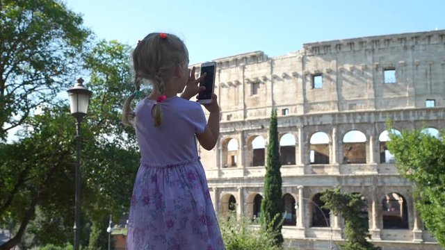 Cute Little Girl in Violet Dress Taking Photos of Coliseum or Colosseum with Smartphone in Rome. Concept of Holidays, Vacations and Travel in Europe