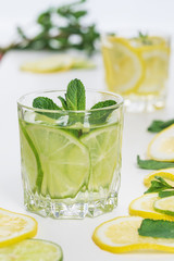 Two glasses of citrus lemonade  with springs of mint and slices of lime and lemon on white table
