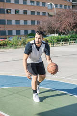 Fototapeta premium Basketball player moves his ball with his left arm while playing on an urban basketball court