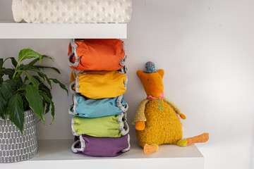 five colored washable diapers stacked on a shelf with a plush and a blanket, horizontal