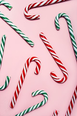 A scattering of red and green striped Christmas candy canes on a pink pastel warm background. New Year seamless pattern, top view. Flat lay. Vertical format