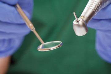 Dentist's hands in glove with dental handpiece and mouth mirror.
