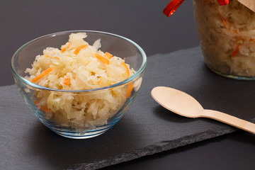 Fermented cabbage with herbs and spices in glass bowl on the black background