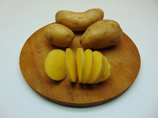 Raw potatoes whole and sliced on a round wooden tray close-up.
