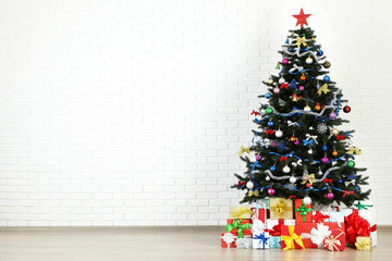 Christmas fir tree with ornaments and gift boxes on white brick wall background