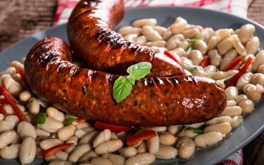 Beans with grilled sausages on wooden background