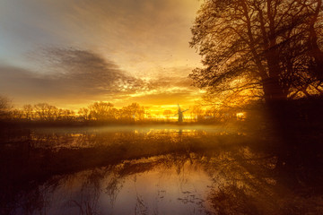 Norfolk windmill in dappled sunrise with mist and floodplain  - Powered by Adobe