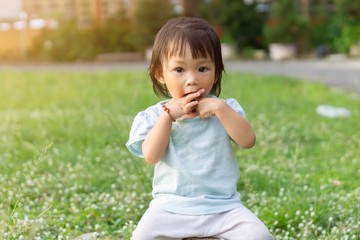 Fototapeta premium Portrait image of baby 1-2 years old. Asian child girl put her hands and in her mouth and biting her fingers at the playground. Personal hygiene and kid healthy concept.