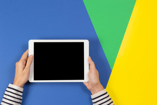 Female hands with digital tablet computer on blue yellow and light green background. Top view