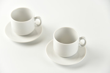 Two white empty cups and saucers on a white background. Selective focus.