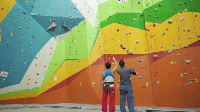 Climbers looking on steep rock, and preparing to climbing on artificial wall indoors. 