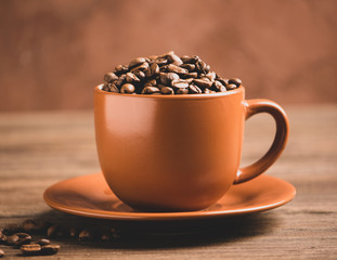 Roasted coffee beans in a brown cup on a wooden background. Coffee energy drink concept. Selective focus. Copy space horizontal frame