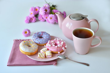 pink teapot, cup of tea and colorful delicious doughnuts